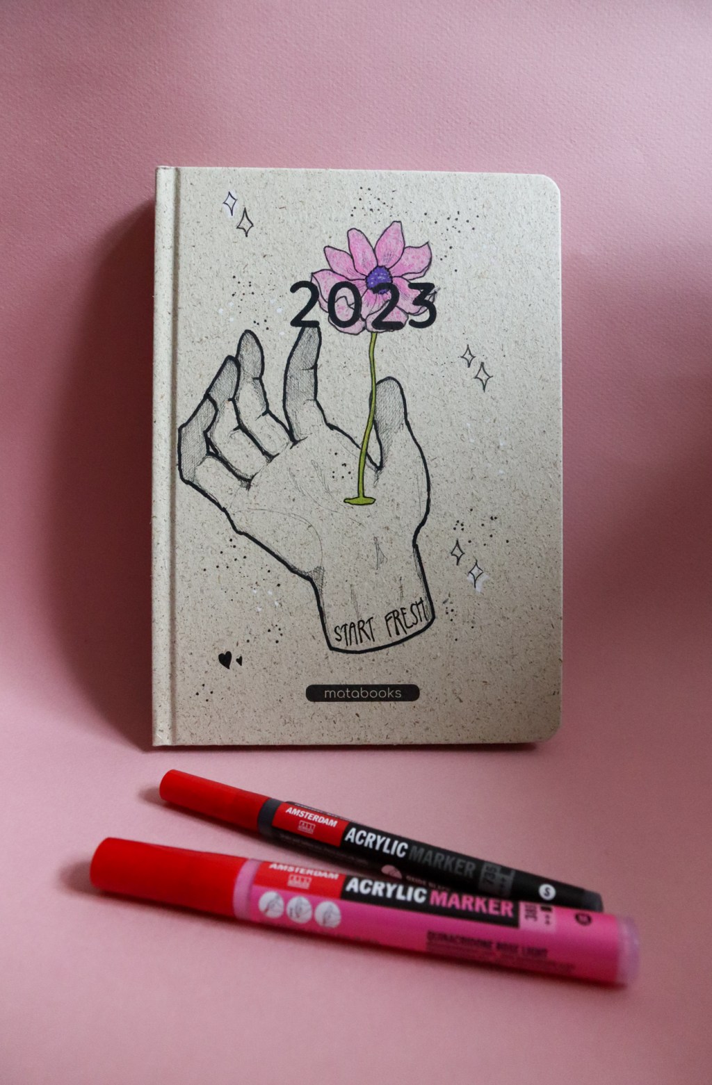 Photo of a matabooks blank calendar 2023 with a drawing by Viktoria Spokojna — a hand with open palm facing up, a flower with pink petals and purple centre growing from it, and the words 